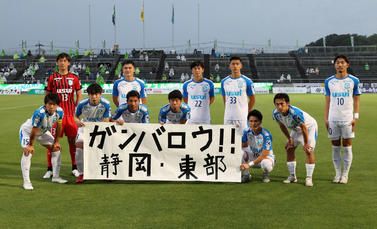 鳥取戦の試合前に「ガンバロウ！！　静岡・東部」と書かれた横断幕を掲げる沼津の選手たち（C）J．LEAGUE