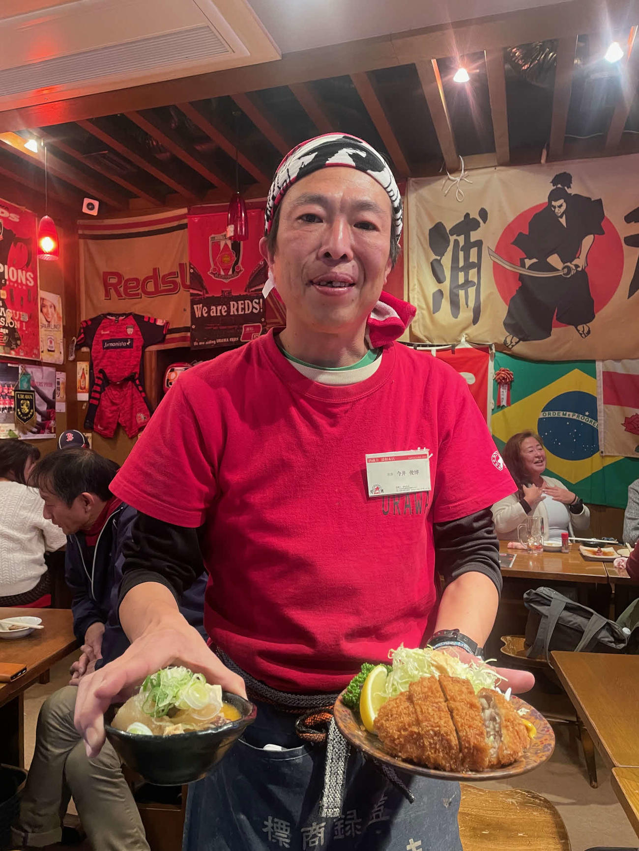 今季限りで現役引退する浦和阿部も愛したモツ煮込みを右手に、左手にメンチカツを手にする浦和ファンの酒蔵　力　浦和本店の今井店長