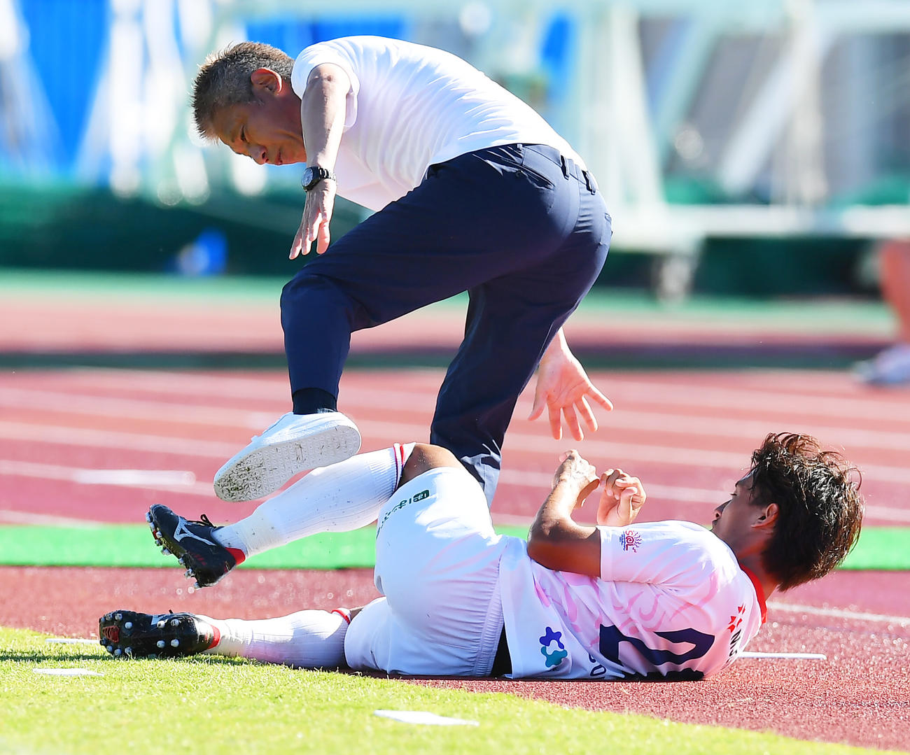 鈴鹿対奈良クラブ　後半、相手選手のタックルが勢いあまってピッチサイドに飛び出し鈴鹿三浦監督（奥）が巻き込まれる（撮影・清水貴仁）