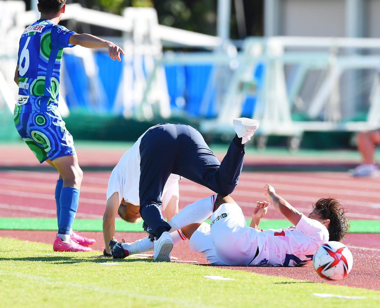 鈴鹿対奈良クラブ　後半、相手選手のタックルが勢いあまってピッチサイドに飛び出し鈴鹿三浦監督（中央）が巻き込まれる（撮影・清水貴仁）