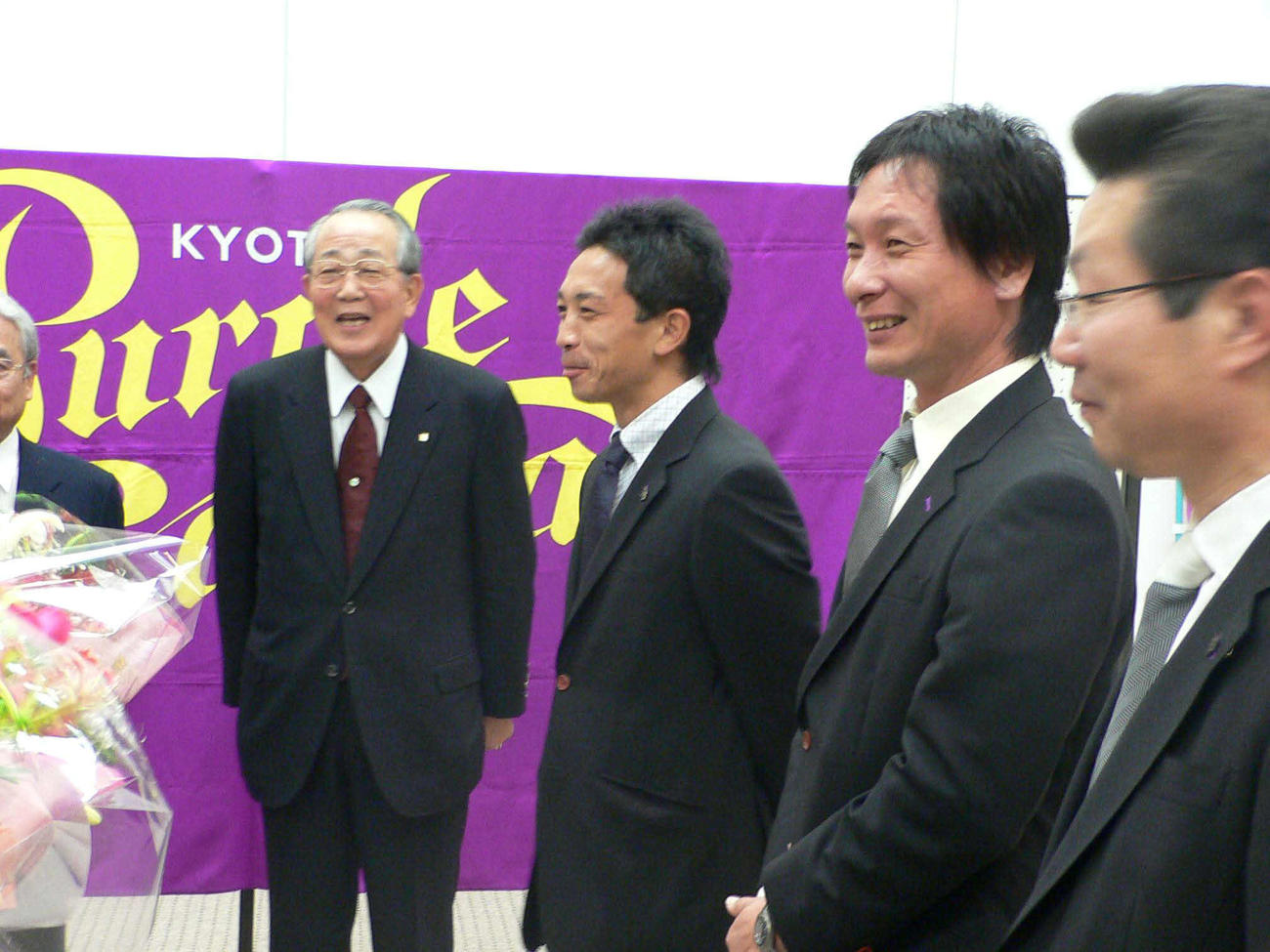 05年、柱谷幸一監督（右から2人目）からJ1昇格の報告を受け笑顔の稲盛名誉会長（左端）