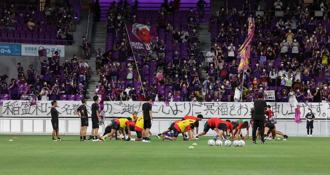 京都対神戸　亡くなった京都サンガF.C.名誉会長の稲盛和夫さんを追悼する横断幕の前でアップを始める京都イレブン（撮影・白石智彦）