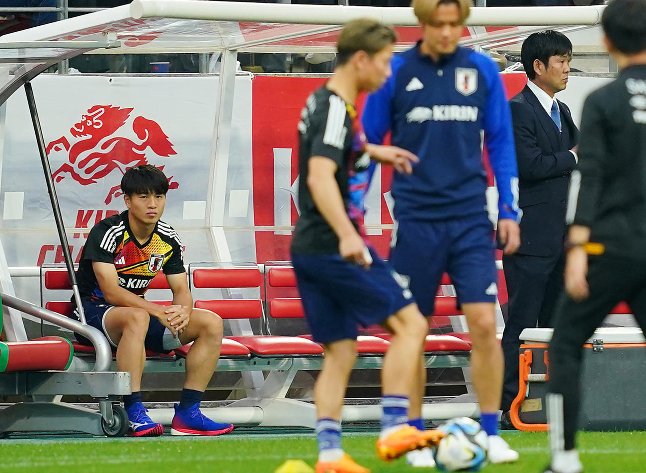 15日、日本代表の試合前練習加わらずベンチに座る川崎颯太（左）