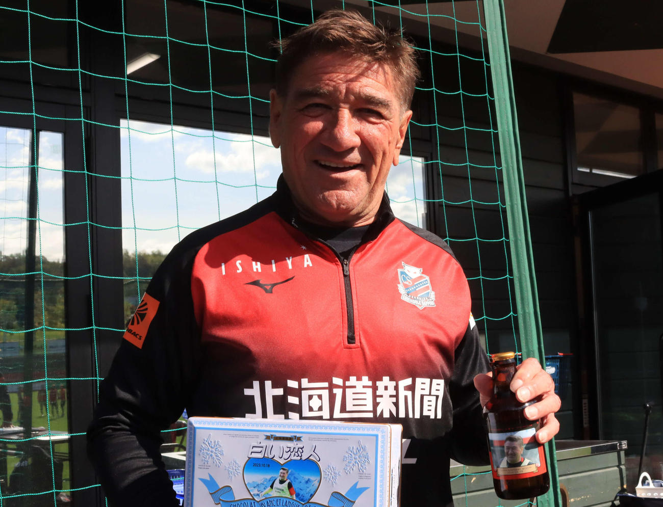 66歳の誕生日を迎えた札幌ペトロビッチ監督は報道陣からプレゼントされた自身の顔写真入りビール瓶と缶を手に笑顔（撮影・保坂果那）