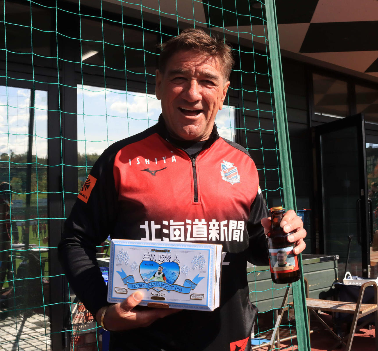 66歳の誕生日を迎えた札幌ペトロビッチ監督は報道陣からプレゼントされた自身の顔写真入りビール瓶と缶を手に笑顔（撮影・保坂果那）