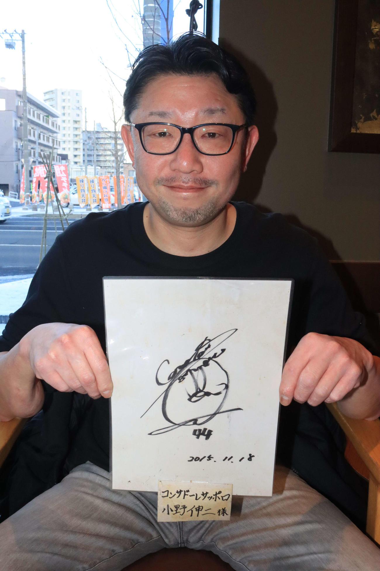 奇跡的に火災で無事だった札幌小野のサインを持つそば辰店長金見さん（撮影・保坂果那）