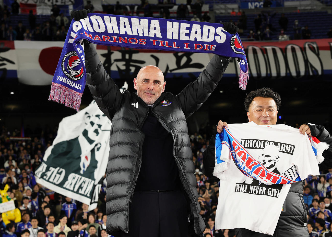 横浜対山東泰山　今季で退任が決まっている横浜マスカット監督（左）はタオルマフラーを広げ笑顔を見せる（撮影・足立雅史）