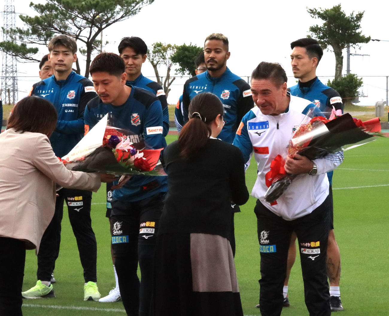 金武町からの歓迎セレモニーで花束を受け取る札幌ペトロビッチ監督（手前右端）。同左から2人目は宮沢（撮影・保坂果那）