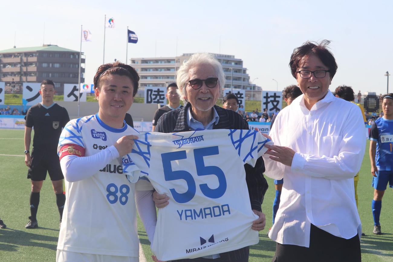 「男はつらいよ」の誕生55周年を記念し、南葛SCのホーム開幕戦に駆けつけた山田洋次監督（中央）はFW大前（左）と高橋陽一代表