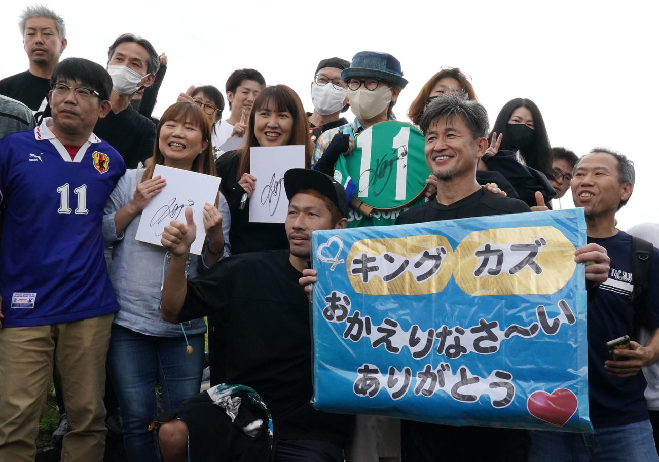全体練習終了後、詰めかけたファンの手にするボードを自ら持ち写真に納まるカズ（前列右）（撮影・森本幸一）