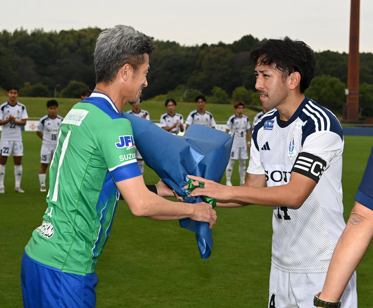 鈴鹿対ソニー仙台　試合前、今シーズンでJFLを退会するソニー仙台吉野主将（右）に花束を手渡す鈴鹿三浦（撮影・前岡正明）