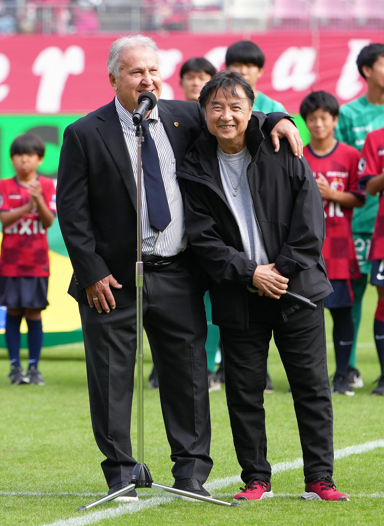 試合前、引退30周年セレモニーであいさつするジーコCA（左）と笑顔を見せる通訳の鈴木氏（撮影・足立雅史）