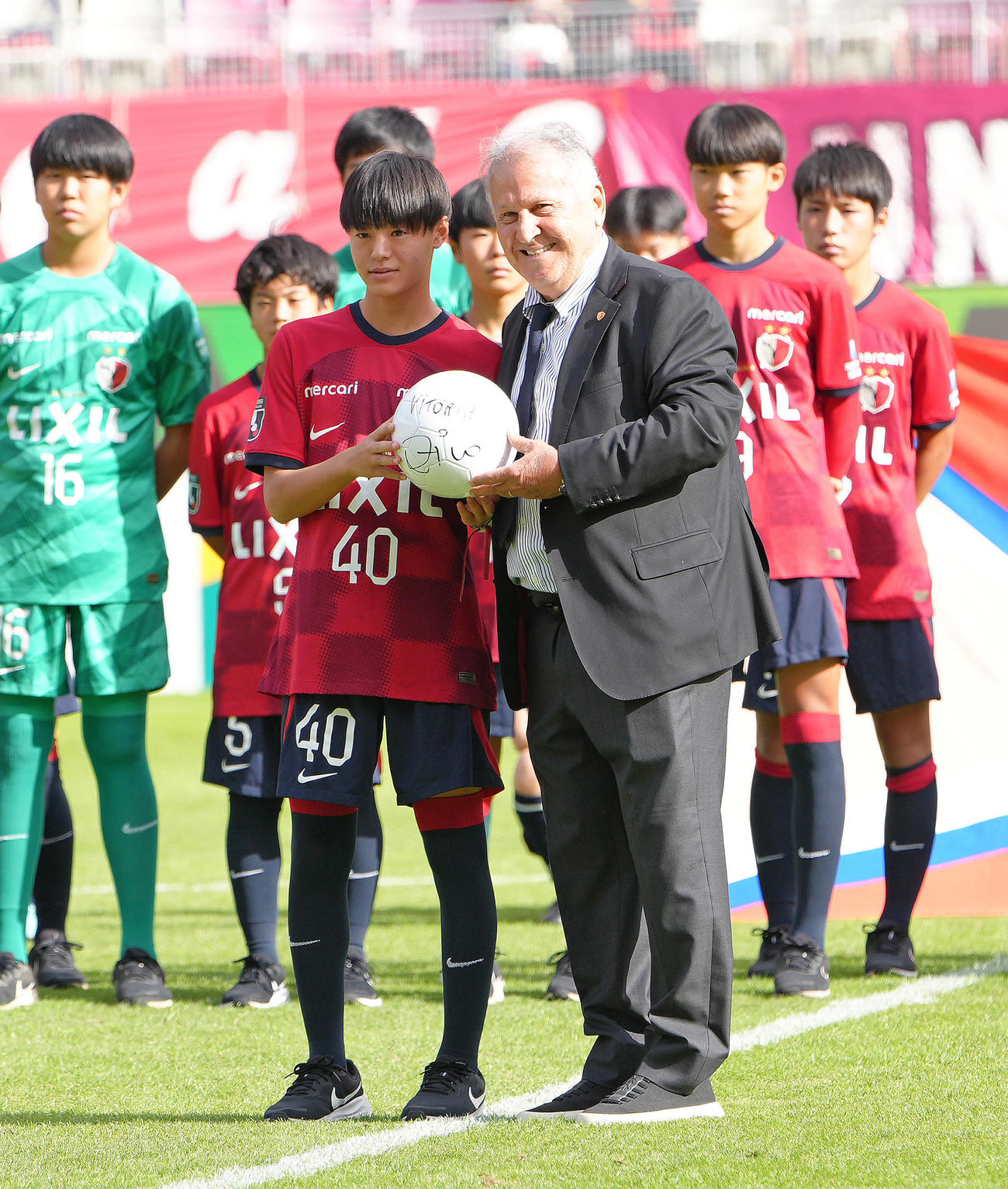 試合前、引退30周年セレモニーを行ったジーコCA（右）からボールを受け取る小笠原満男氏の長男で鹿島ジュニアユースの小笠原央（ひろ）（撮影・足立雅史）