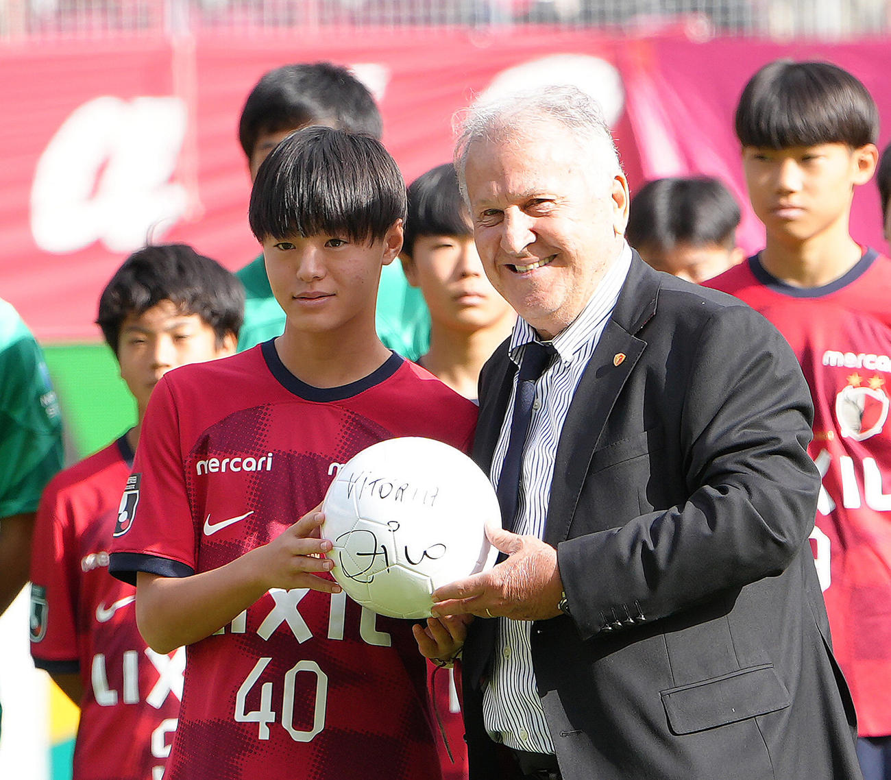 試合前、引退30周年セレモニーを行ったジーコCA（右）からボールを受け取る小笠原満男氏の長男で鹿島ジュニアユースの小笠原央（ひろ）（撮影・足立雅史）