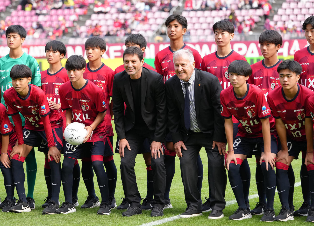 試合前、引退30周年セレモニーを行ったジーコCA（中央右）と笑顔で記念撮影する、前列左から、1人おいて小笠原満男氏の長男で鹿島ジュニアユースの小笠原央（ひろ）、レオナルド氏ら（撮影・足立雅史）