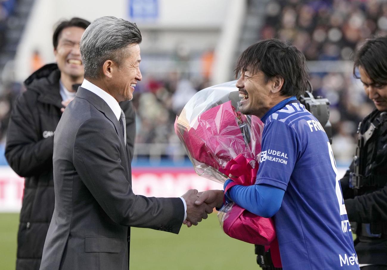 松井大輔引退試合　引退試合を終え、鈴鹿・三浦から花束を贈られ笑顔の松井大輔（右）（共同）
