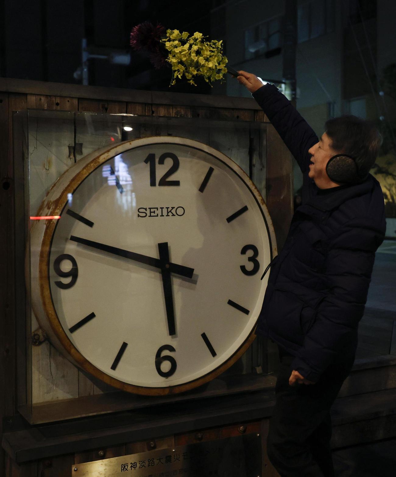 阪神大震災から30年の朝を迎え、発生時刻で止まったままの大時計に花を手向ける男性＝17日早朝、兵庫県西宮市（共同）
