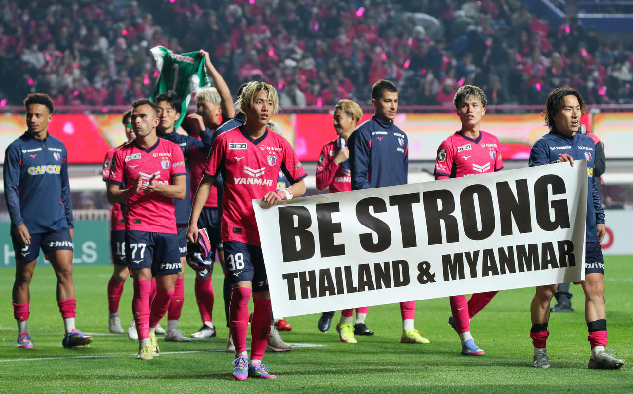 試合後、ミャンマー大地震を悼み「BE　STRONG」の横断幕を持ちピッチをピッチを歩くC大阪北野（手前左）と登里（右）（撮影・上山淳一）