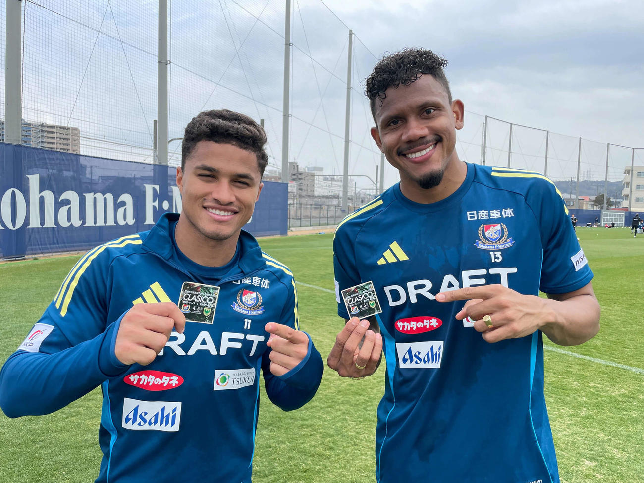 横浜のヤンマテウス（左）とキニョーネスは来場者に配布されるステッカーを手にする（横浜F・マリノス提供）