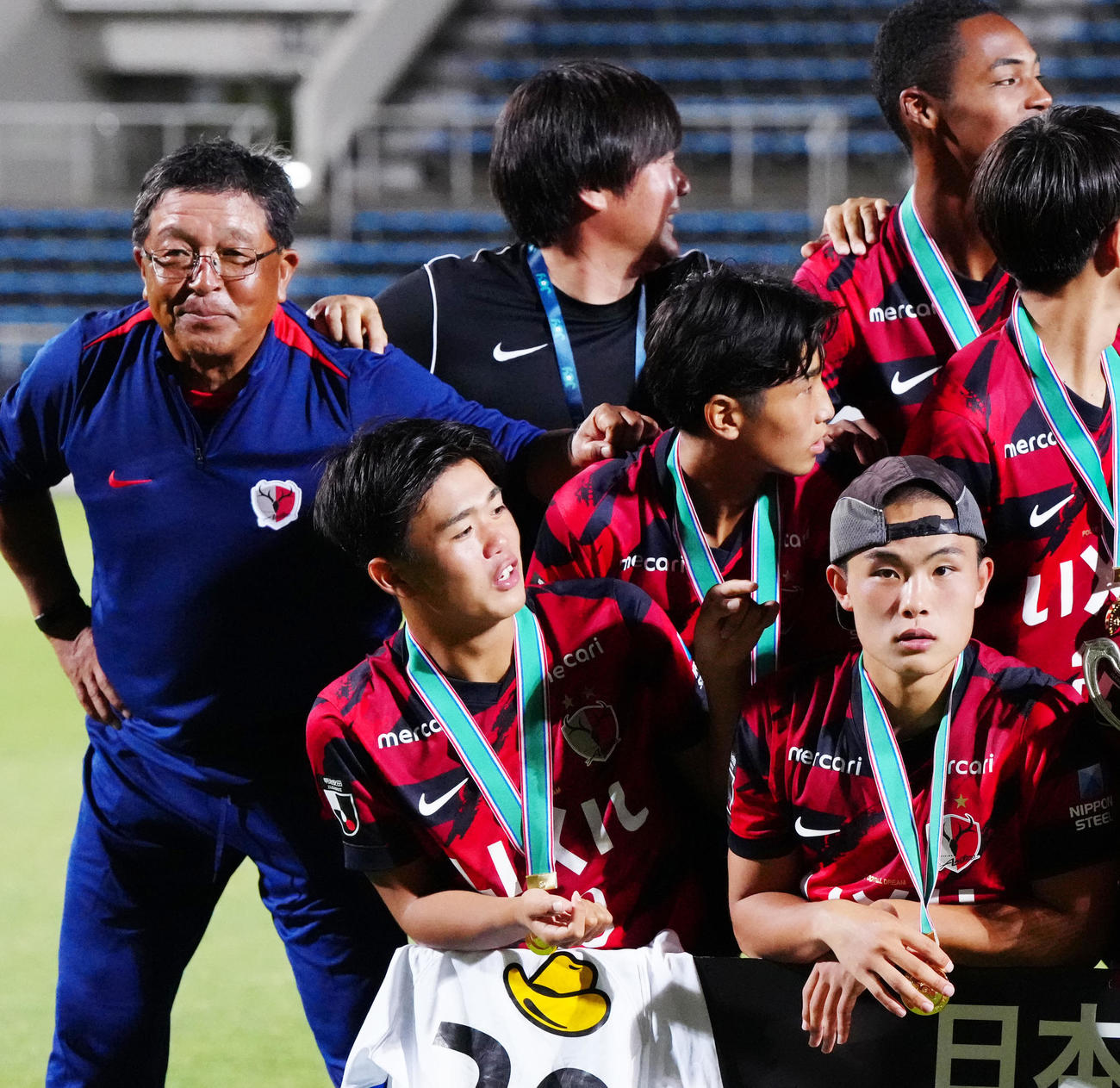 日本クラブユースサッカー選手権（U－18）大会　決勝　鹿島ユース対仙台ユース　優勝記念写真撮影で里内猛氏（左）の帽子をかぶる吉田湊海（右下）（2025年7月31日撮影）