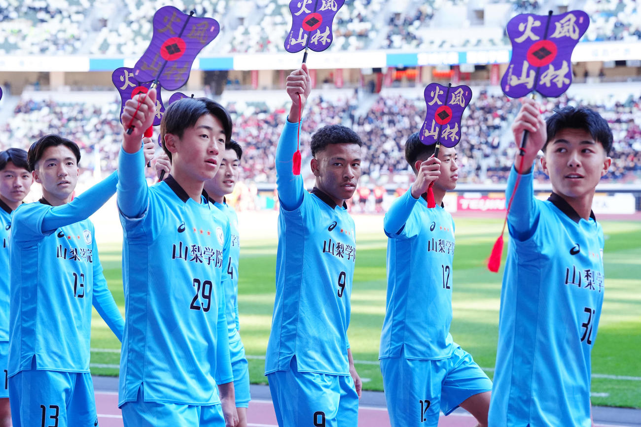 全国高校サッカー選手権の開会式で「風林火山」の文字が入った軍配を手に行進した山梨学院の選手たち（撮影・江口和貴）
