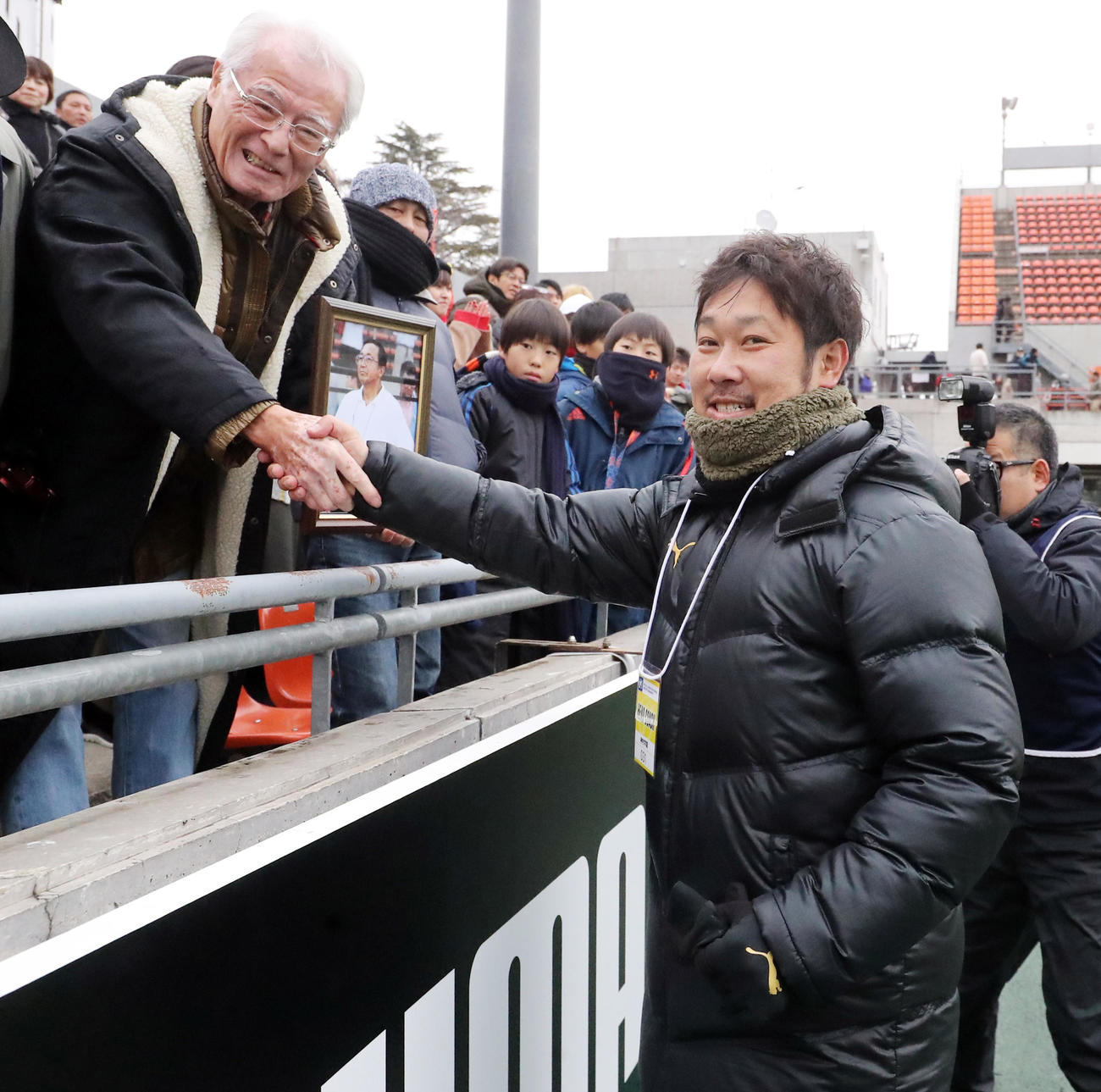 2017年12月、就任1年目の神村学園有村監督（右）は、亡くなった恩師の故・松沢総監督の遺影を持った関係者と笑顔で握手