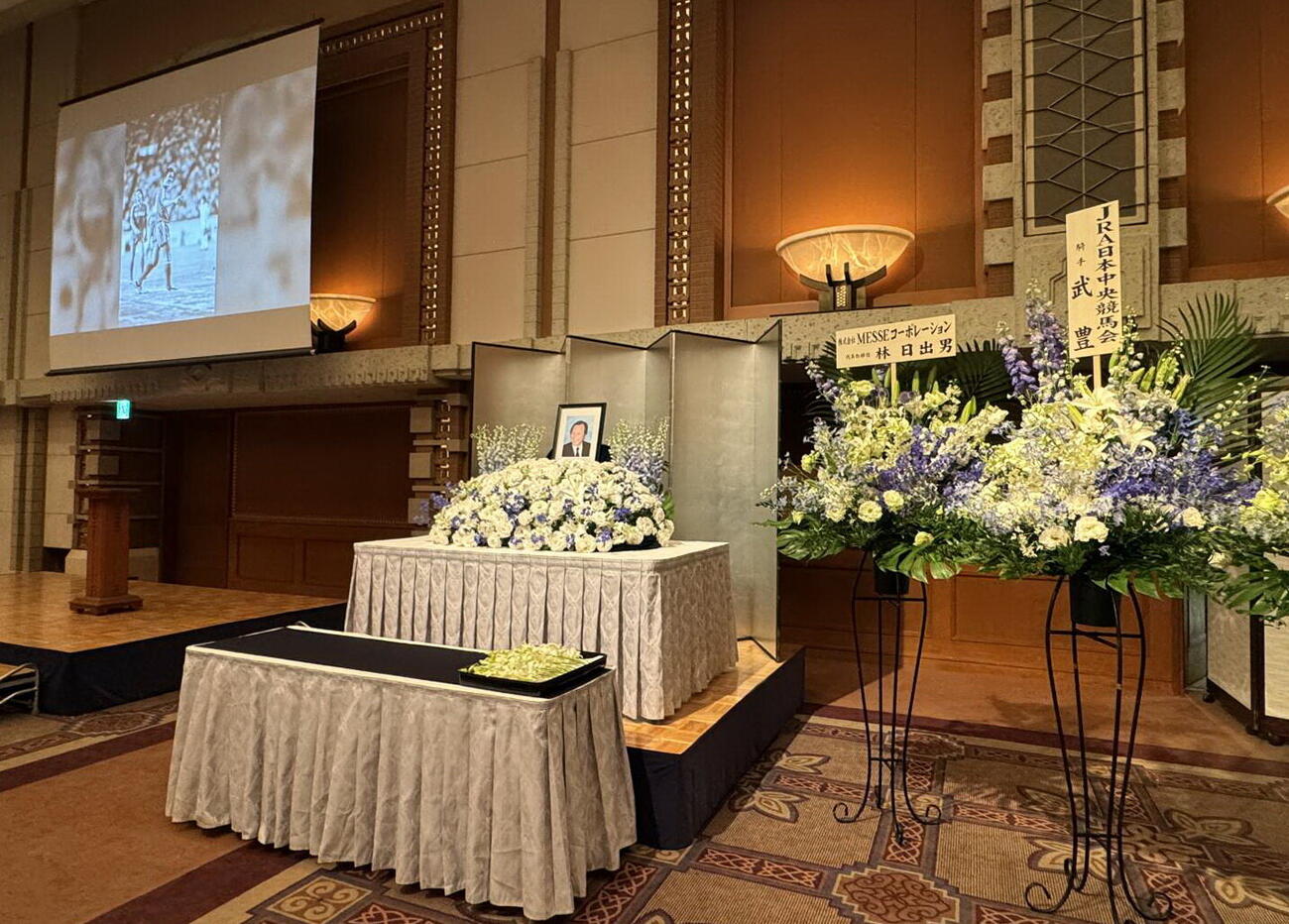 釜本邦茂さん一周忌の会場には祭壇や生花がかざわれ壇上にはスライド写真も（家族提供）