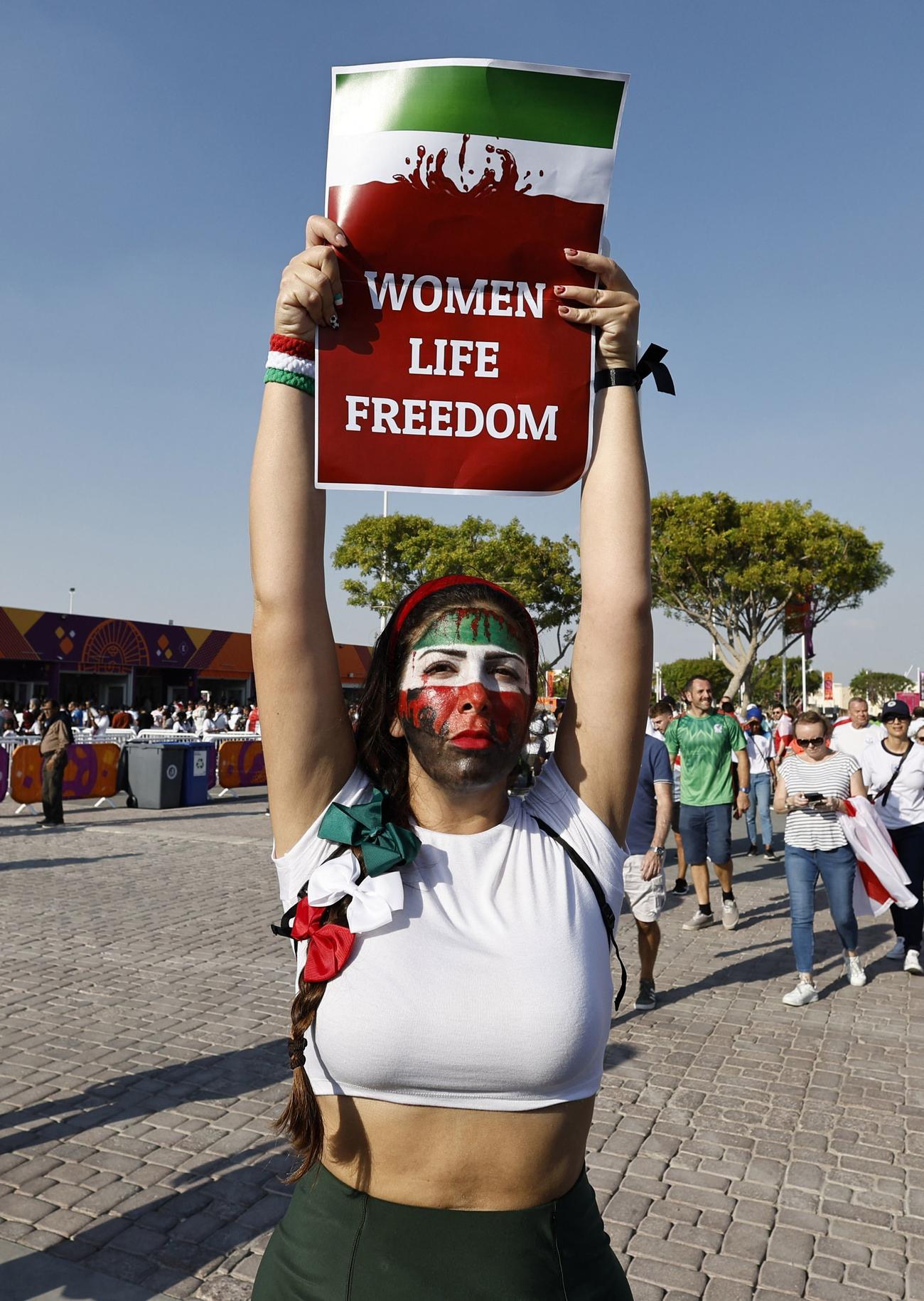 試合前にスタジアム外で「Woman life freedom」と書かれた看板を持つ女性（ロイター）