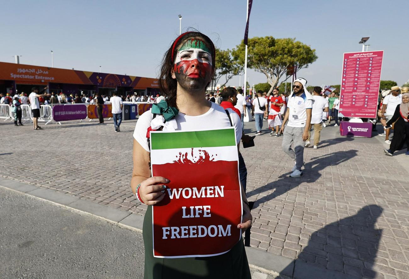 試合前にスタジアム外で「Woman life freedom」と書かれた看板を持つ女性（ロイター）