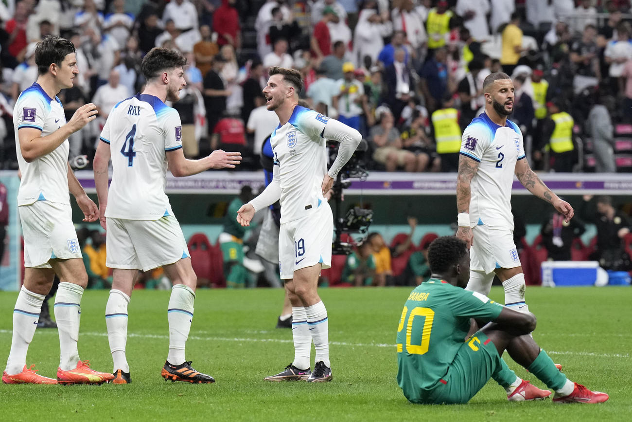 イングランド－セネガル戦、試合に敗れ座り込むセネガルのバンバ・ディエンと勝利を喜ぶイングランドの選手たち（AP）