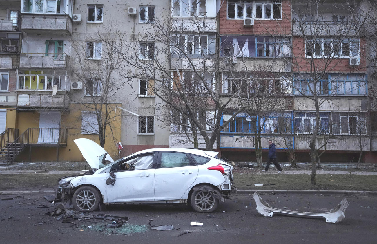 ロシアの砲撃を受けて破損した車両と瓦礫の前を歩くウクライナの男性（AP）