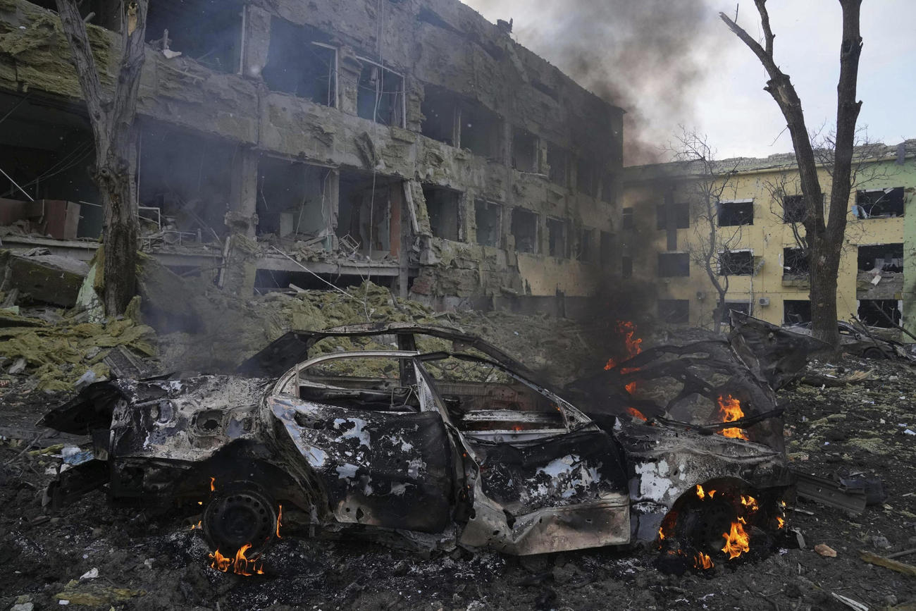爆撃でこわれた病院と、もえる車。出産のための病院がロシア軍の攻撃を受けた＝3月9日、ウクライナ・マリウポリ（AP＝共同）