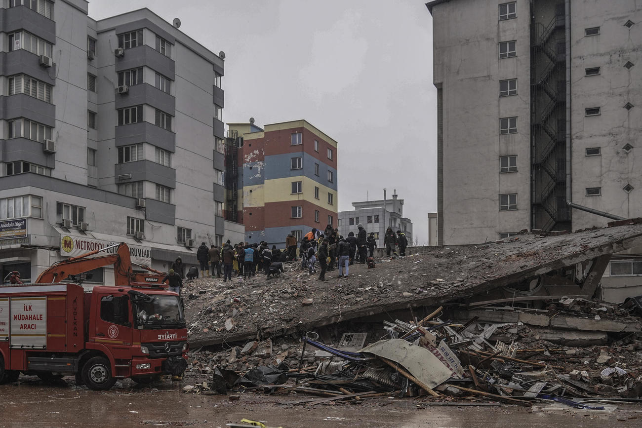トルコのガズィアンテプで破壊された建物のがれきの中を捜索する人々たち(AP）