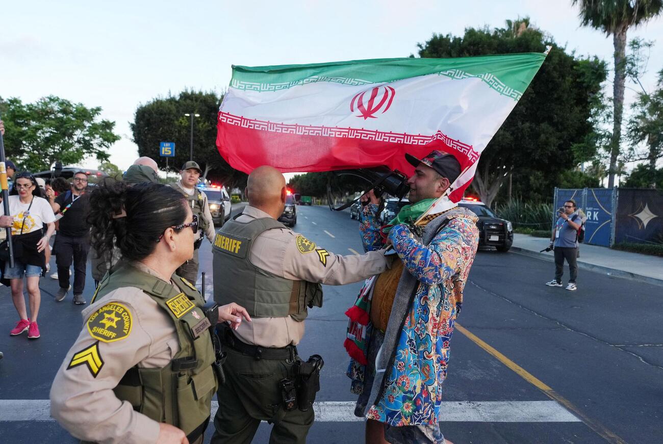 スタジアムの外で、旗を振りメガホンを使って叫ぶ親イラン政権の抗議者と、警察官がやり取りしている様子（ロイター）