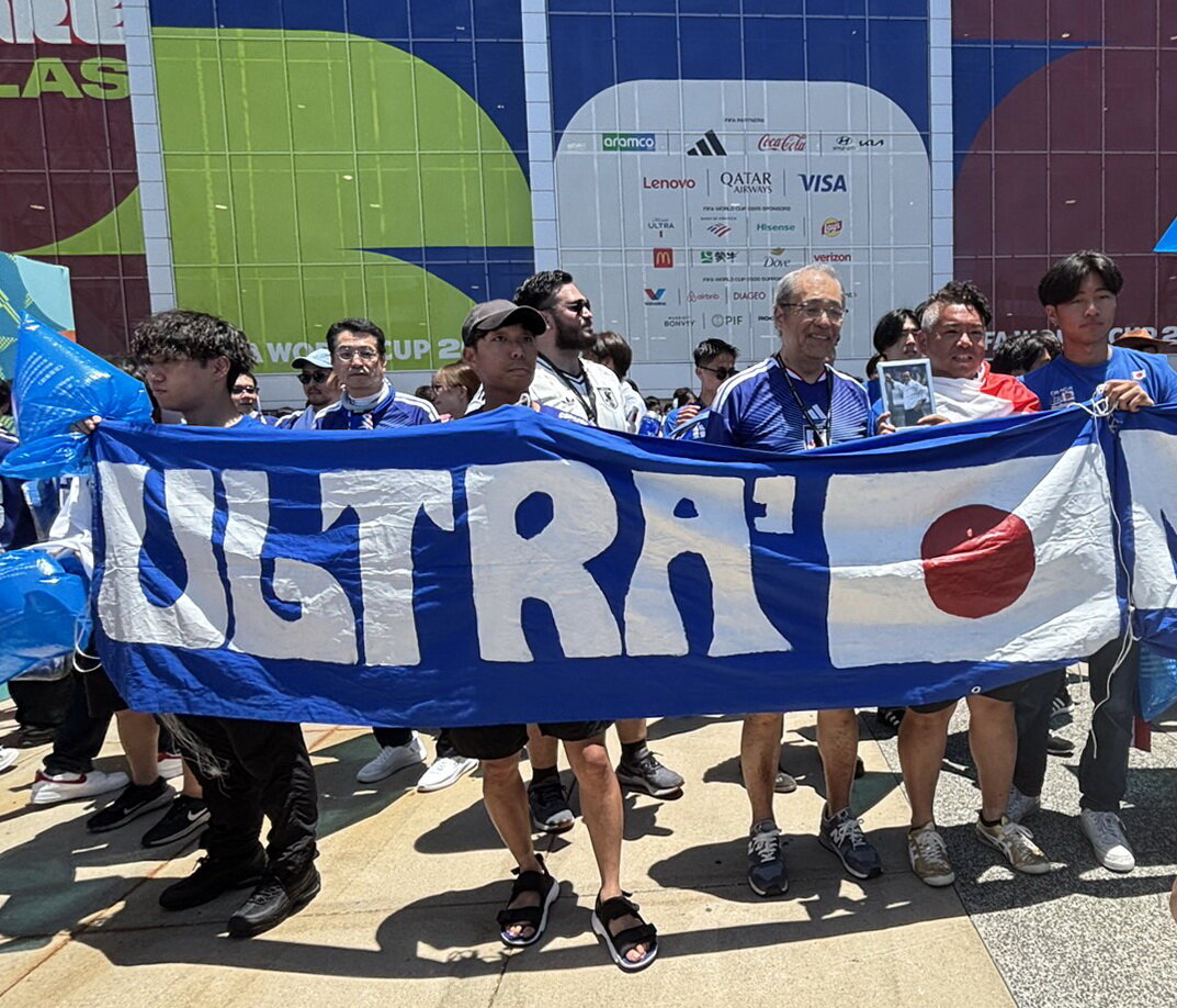 14日、日本のW杯初戦、オランダ戦の会場で釜本邦茂さんの遺影を持ってサポーターと交流する坂井信幸さん（清仁会シミズ病院坂井信幸院長提供）