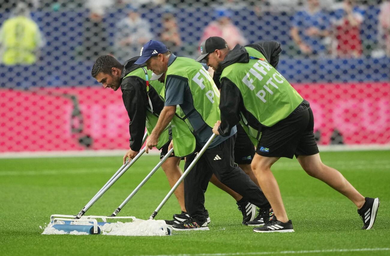 雷雨警報により試合が遅延する中、グラウンドキーパーがピッチの整備作業を行う（ロイター）