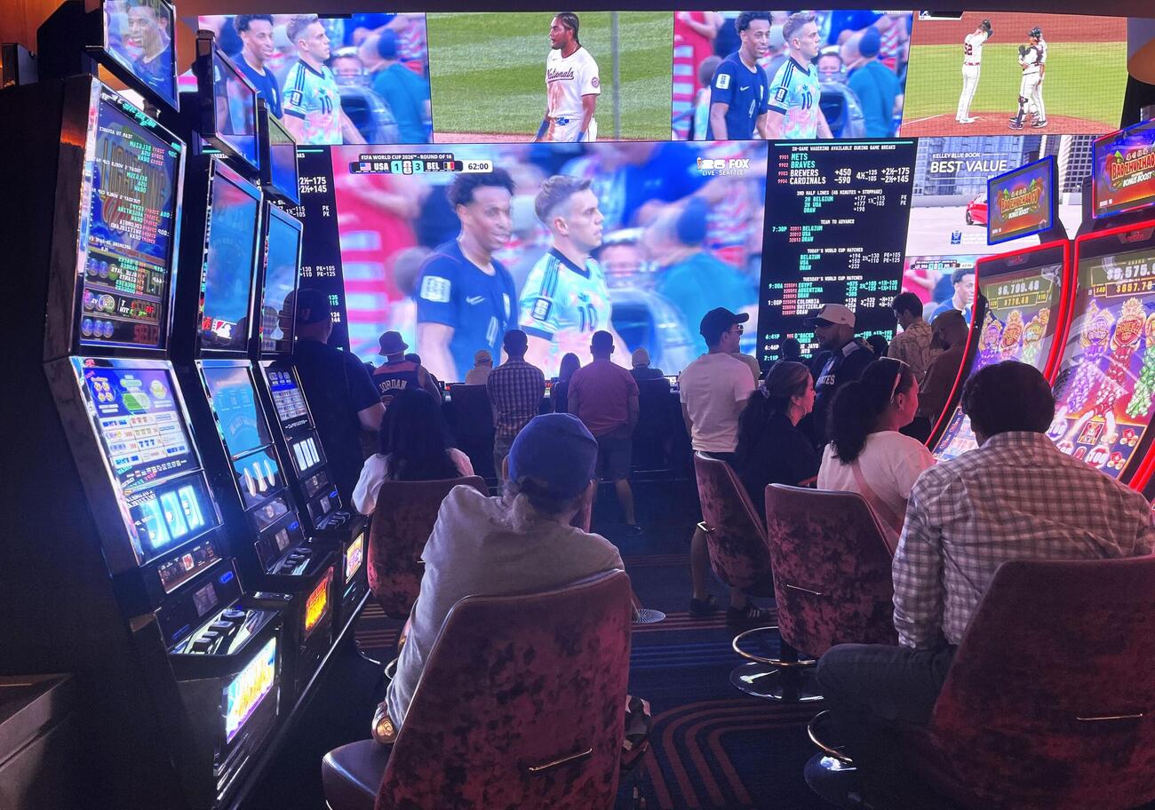 6日、米ラスベガスのカジノでスロットマシンの前からサッカーW杯の試合を見る人たち（共同）