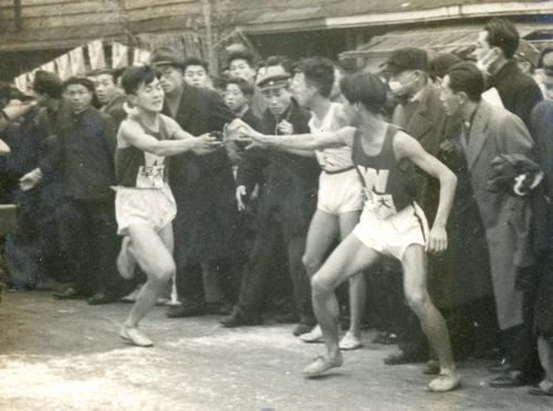 第26回大会　往路2区鶴見中継所　1区田辺時夫（左）から2区篠田正浩（右＝のち映画監督）へ5位でタスキリレーする早大、篠田正浩は1時間13分20秒で区間5位ながら順位を1つ上げ4位で3区へ（1950年1月5日）