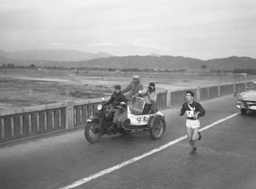 第33回大会　往路4区　サイドカーからの激励を受けピッチを上げるトップを行く日大・松川行毎（1957年1月2日）