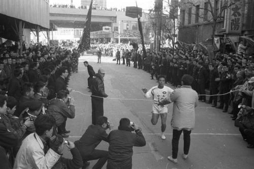 第38回大会　復路10区読売新聞社横ゴール　区間新の1時間7分22秒でゴールに飛び込む中大のアンカー横溝三郎（4年）、1区からトップを守り続けた中大は2位明大に12分08秒差をつけ4年連続（大会タイ）11度目の優勝（1962年1月3日）