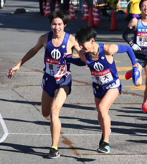 戸塚中継所で順大の2区塩尻（左）からたすきを受け走り出す3区橋本（撮影・足立雅史）