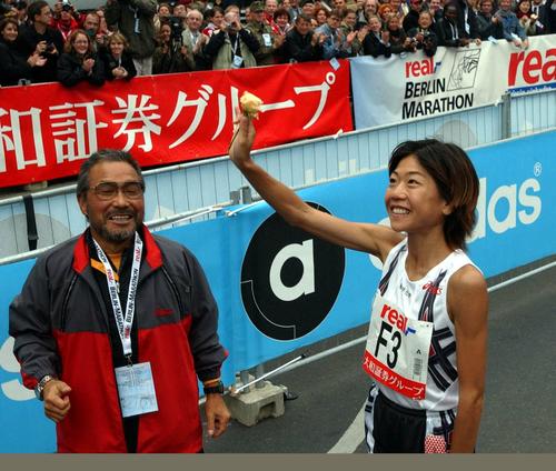 2002年9月29日、ベルリンマラソン2連覇した高橋尚子はゴールの後、黄色いバラを上げ声援にこたえる。左は小出義雄監督