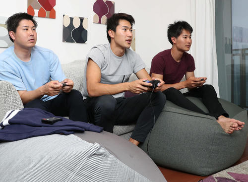 飯塚（中央）は次男裕也さん（左）、三男拓巳さんと真剣な表情でテレビゲームを行う（撮影・松本俊）