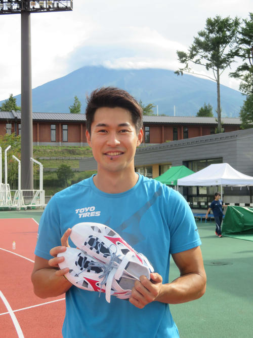 富士山をバックに、白と赤の新色スパイクを手にする飯塚（撮影・上田悠太）
