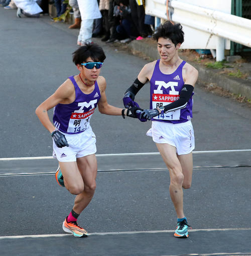 鶴見中継所で明大2区加藤（左）にたすきを渡す明大1区小袖（撮影・大野祥一）