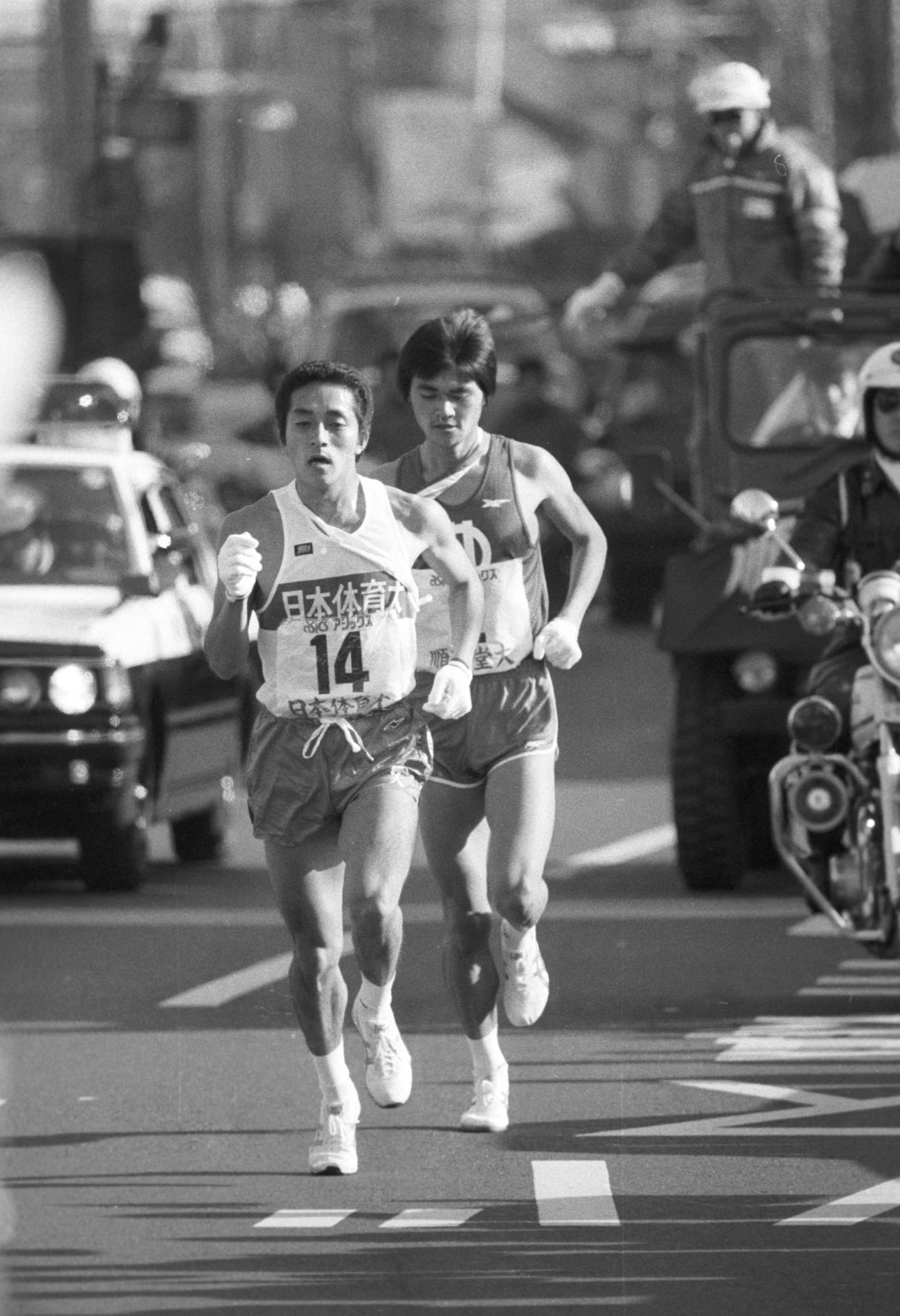 往路2区　鶴見中継所で46秒差でタスキをもらった日体大・大塚正美（手前＝3年、区間1位）は、浦島ケ丘歩道橋で順天堂大・中井良晴（後ろ＝3年、区間4位）とらえ、11キロ地点で抜き去る　　※日体大はこの日、選手変更締め切り時間7時20分の1秒前に「2区を大塚に、5区を岡に」の奇襲作戦に出た＝1982年1月2日