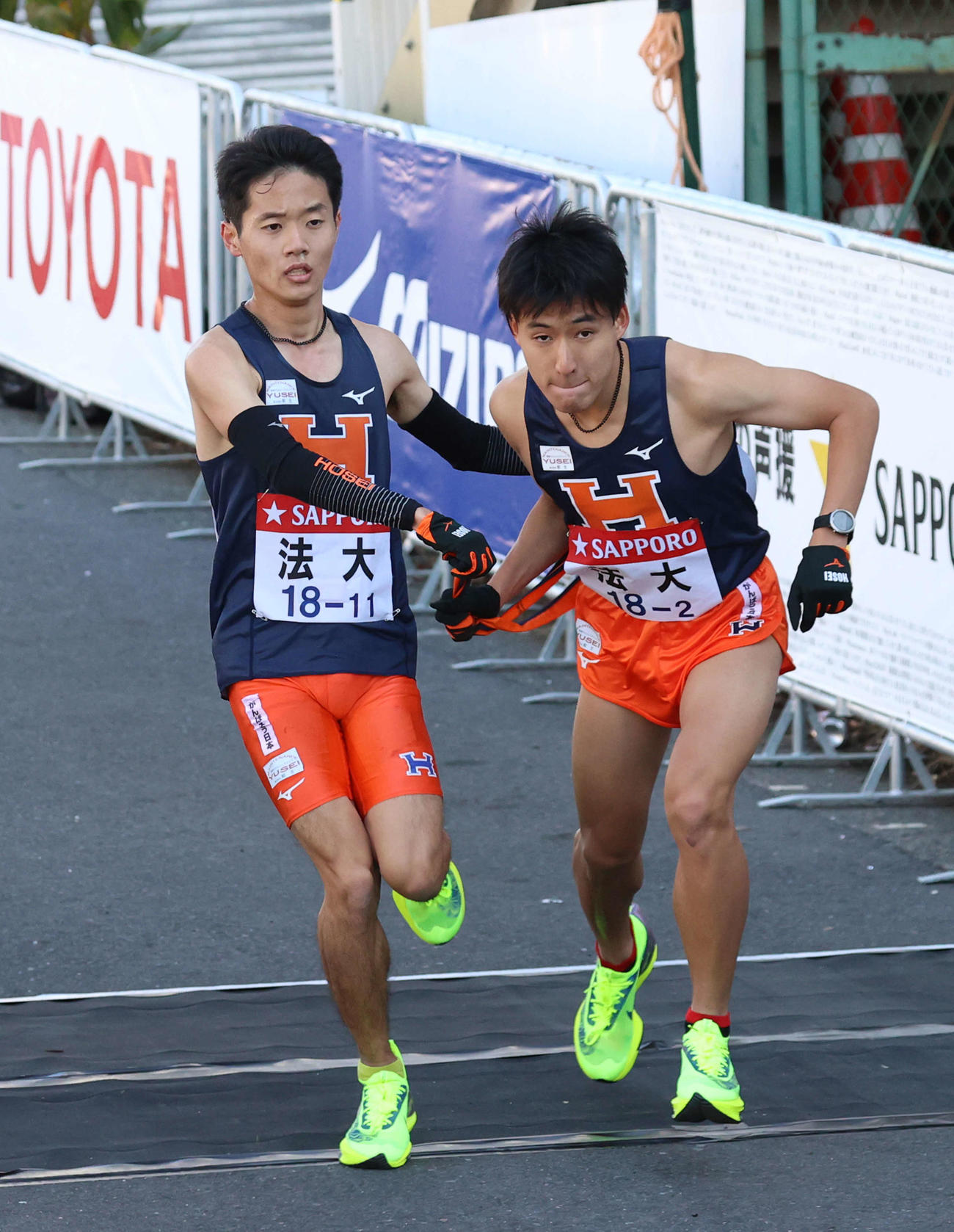 鶴見中継所、トップでタスキをつなぐ法大1区鎌田（左）と2区河田（撮影・河野匠）