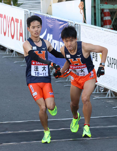 鶴見中継所、トップでタスキをつなぐ法大1区鎌田（左）と2区河田（撮影・河野匠）