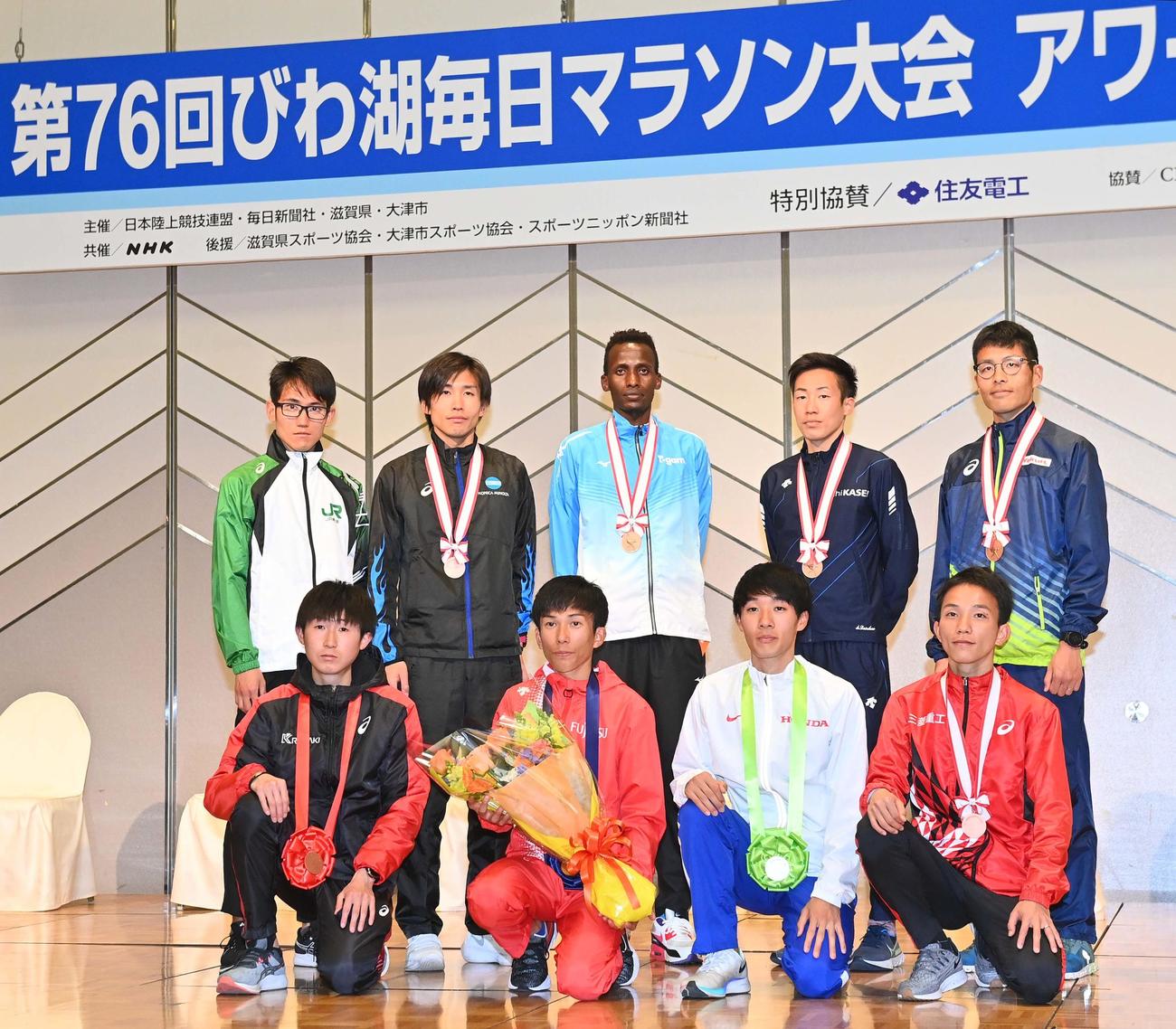 びわ湖毎日マラソン大会アワードセレモニーで記念撮影する下段左から3位・細谷恭平、1位・鈴木健吾、2位・土方英和、4位・井上大仁、上段左から新人賞の作田将希、8位・菊地賢人、7位・S.カリウキ、6位・大六野秀畝、5位・小椋裕介（撮影・上田博志）