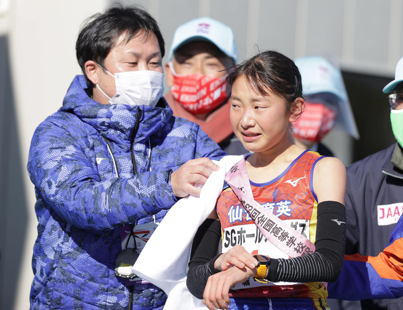 1位でゴールし、仙台育英・釜石監督（左）からタオルを掛けてもらうアンカー須郷（撮影・前田充）